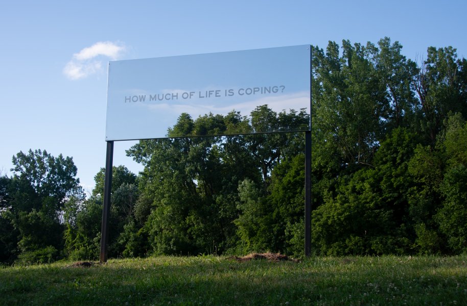 Reflective signage that reads How Much of Life is Coping. Sign is installed in a park-like scenery