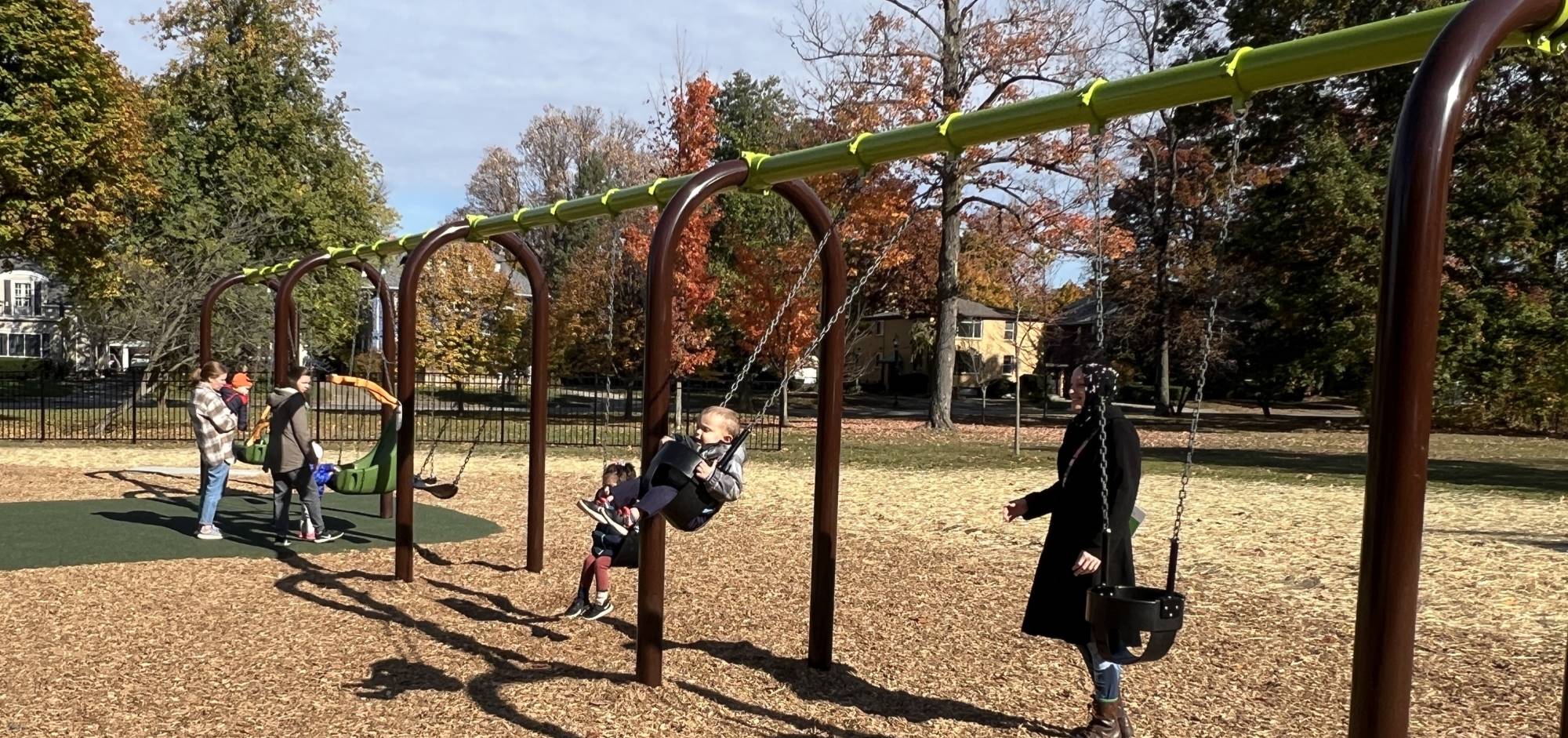 Swing equipment with one child in the far left and another child in the second swing from the right. Both children had adult supervision.