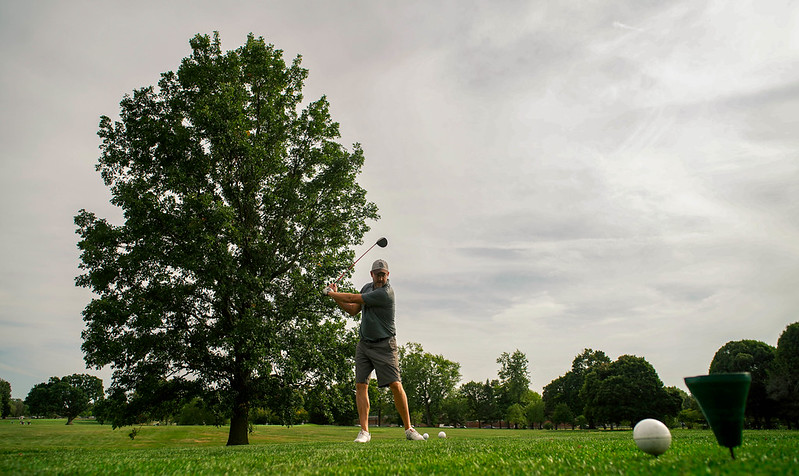 Large tree in the background with a golfer hitting a golf ball