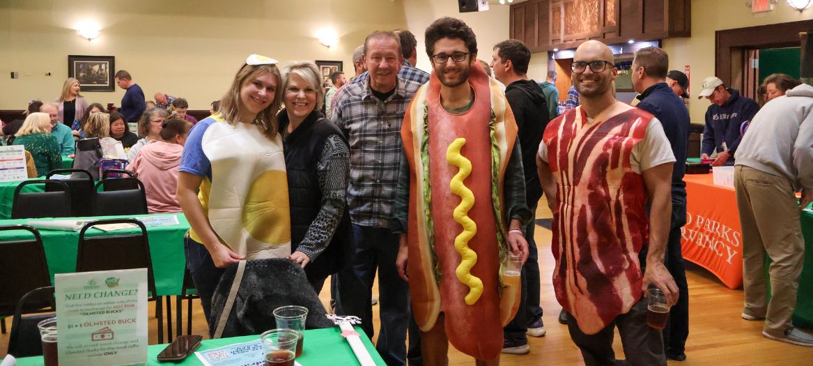 Individuals posing for a photo, a woman in an egg suit, a man in a hotdog suit and another man in a bacon suit